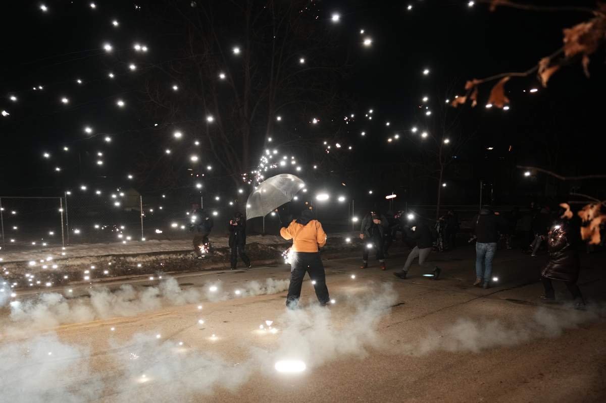 A protester holds an umbrella as sparks fly from a flash bang deployed by law enforcement on Wednesday, Jan. 14, 2026, in Minneapolis.