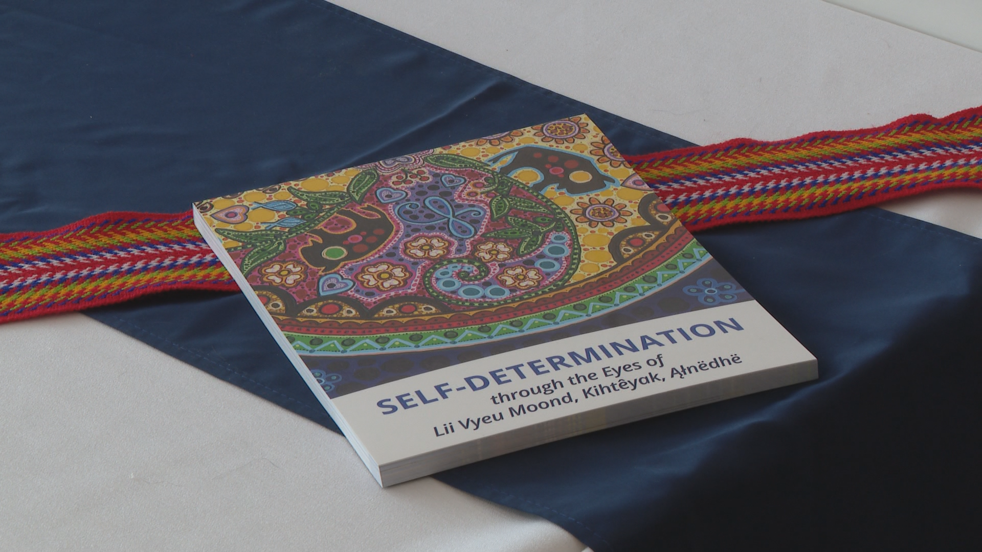 A book with a colourful cover sits on a table with a blue table cloth and red banner that runs across it.
