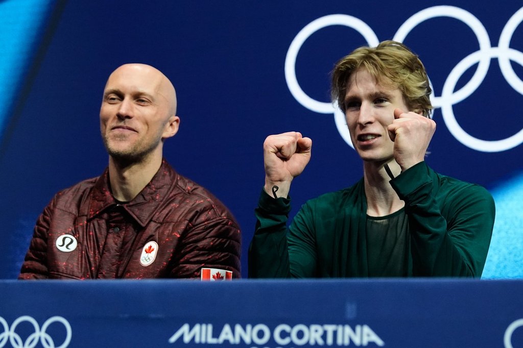 Stephen Gogolev of Canada, right, reacts to his scores after competing during the men's free skate program in figure skating while sitting next to choreographer Benoit Richaud, left, at the 2026 Winter Olympics, in Milan, Italy, Friday, Feb. 13, 2026. (AP Photo/Ashley Landis).