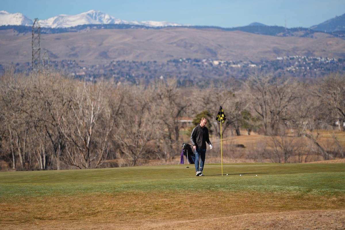With snow covering the mountain backdrop, a lone golfer putts out on a green on the Broken Tee Golf Course, Friday, Feb. 6, 2026, in Sheridan, Colo.