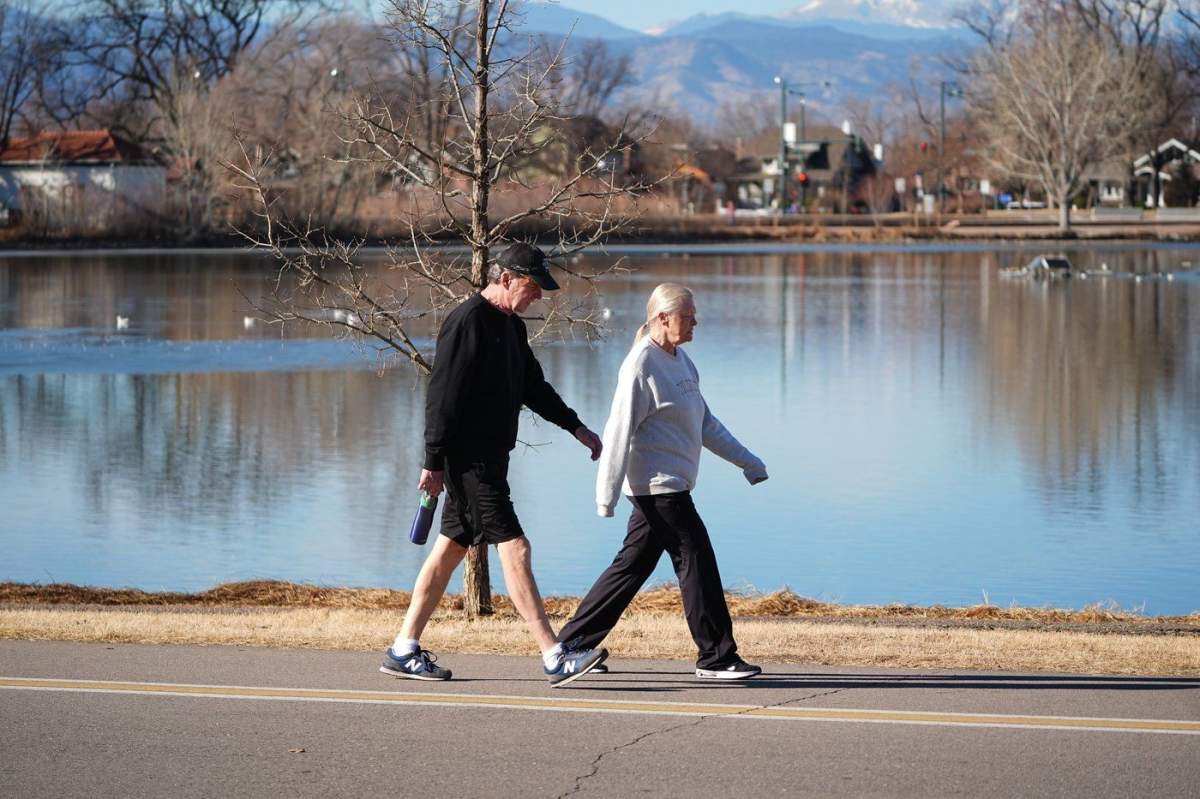 With a backdrop of snowless mountains, a couple walk around the lake in Denver's Washington Park on Friday, Feb. 6, 2026.