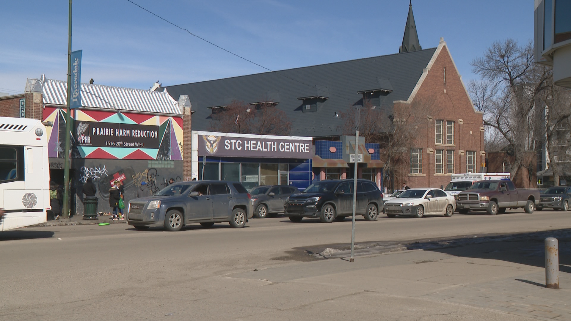 A colourful building on a wide street with a sign reading Prairie Harm Reduction is next to two other buildings against a bright blue sky.
