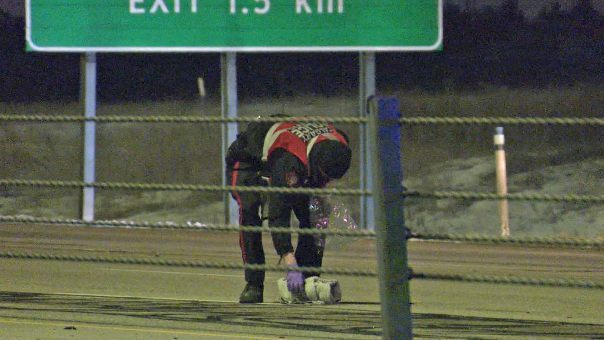 A member of the Calgary police collision reconstruction team is seen examining what appears to be a pair of shoes, after a pedestrian was killed on Stoney Trail northeast, late Tuesday night.