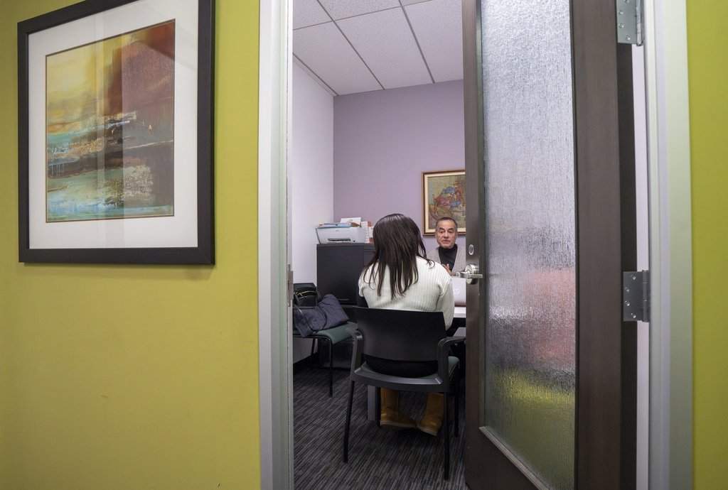 Frantz André, facing, spokesperson for Comite d'action des persons sans statut (CAPSS), speaks to a Haitian migrant, who did not want to be identified and who recently crossed the border from the United States, in his offices in Montreal on Wednesday, Feb. 4, 2026. THE CANADIAN PRESS/Christinne Muschi.