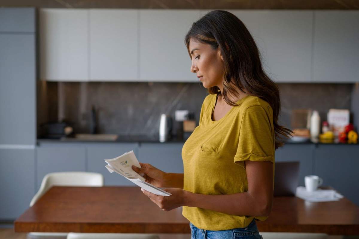 Woman at home reading a letter in the mail and looking serious.